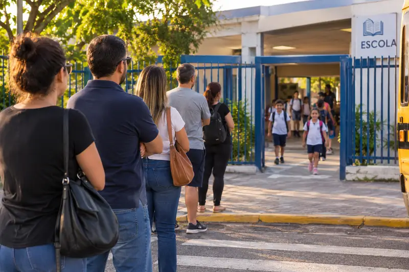 Pais em fila na calçada esperando os filhos saírem pelo portão da escola